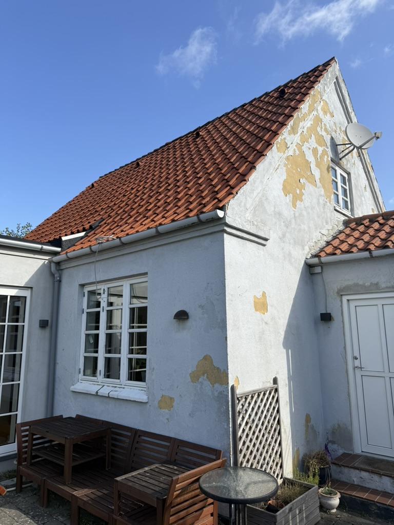 Rødt tegltag på hvid villa med sadeltag og terrasse